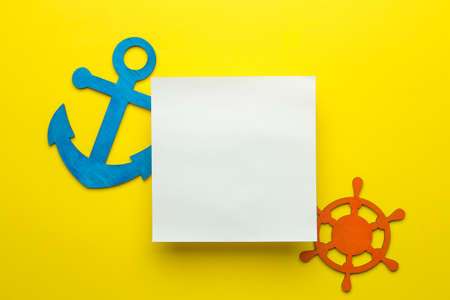 Summer frame. paper frame for your text, decorative sea anchor and steering wheel on a bright yellow background. top viewの写真素材