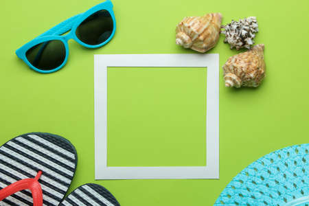 Summer frame. Paper frame for your text, flip flops, glasses and seashells on bright green background. top viewの写真素材