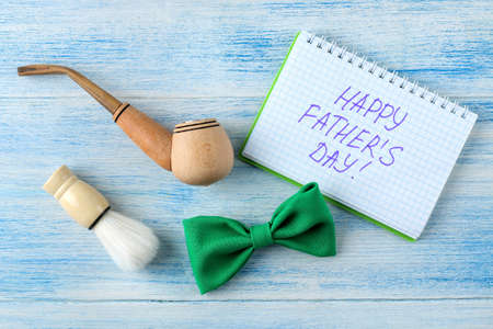 happy father's day. text and decorative men's tie butterfly and smoking pipe on a light blue wooden background. top viewの写真素材