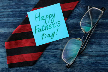 Happy father's day. text on paper and man's tie and glasses on a blue wooden table. men's holiday. top viewの写真素材