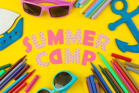 Text SUMMER CAMP of multicolored paper letters and colored felt-tip pens on a bright yellow...