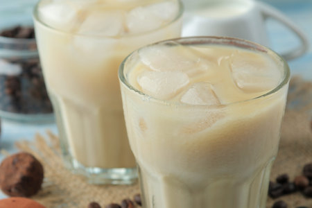 iced coffee with milk and ice cubes in a glass cup on a light blue background. refreshing drink....
