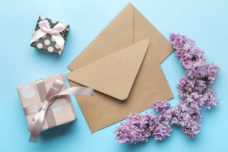 Craft envelope with a sprig of lilac and gift box on a bright trendy light blue background. top view