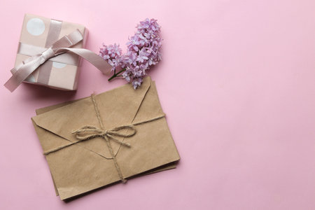 Craft envelope, lilac branch and gift box on a bright trendy pink background. top view