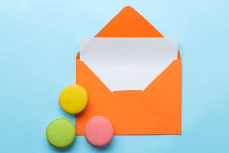 Orange envelope with an inscription letterhead and macarons cake on a bright trendy light blue background. top viewの写真素材