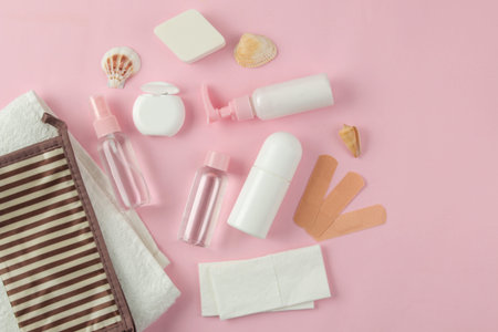 A set of cosmetics and personal care products for travel in a cosmetic bag on a light pink...