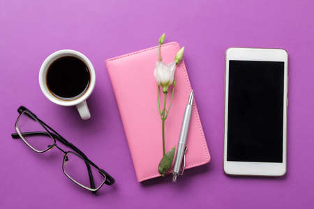 Notepad and glasses cup of coffee and flowers and a smartphone on a bright lilac background. top view. office toolsの写真素材