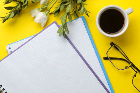 several notebooks and glasses a cup of coffee and flowers on a bright yellow background. top view. office toolsの写真素材