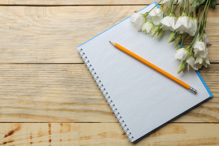 Notebook with a pencil and white flowers on a natural wooden table. top view