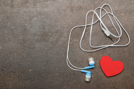 Small blue headphones for a smartphone and a decorative heart on a dark background. top view. free...