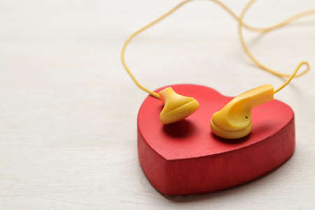Small yellow headphones and red decorative heart on a white wooden background.の写真素材