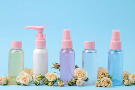 Cosmetics for face and body in pink bottles with fresh roses on a gentle blue background. creams and lotion. spa.の写真素材