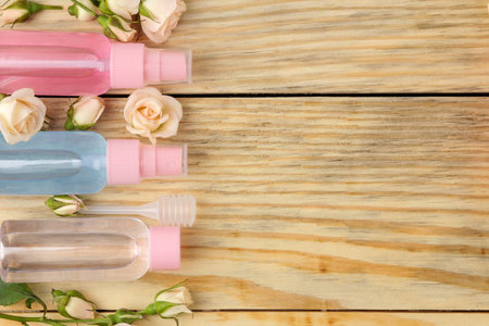 Face and body cosmetics in pink bottles with fresh roses on a natural wooden background. creams and...