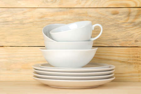 Piles of white ceramic tableware, plates, saucers and cups on a natural wooden background. kitchenware.の写真素材