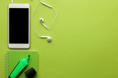 Smartphone White phone and earphone and notepad on a bright green background. top view. space for...