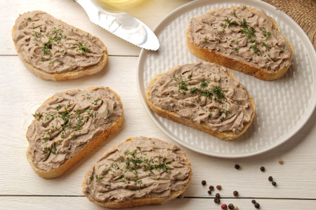 Fresh homemade chicken liver pate with herbs for bread on a white wooden table. A sandwich. top view