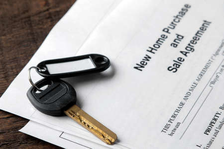 new home purchase and sale agreement. Key with keyring and blank on a brown wooden table. concept of buying a home.の写真素材