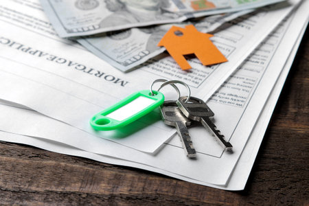 mortgage application. Key with house key fob and blank and money on a brown wooden table. concept of...