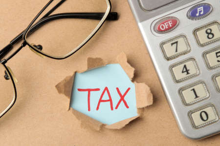 The word tax and torn paper, glasses, calculator. Taxes on the background of craft paper. top viewの写真素材