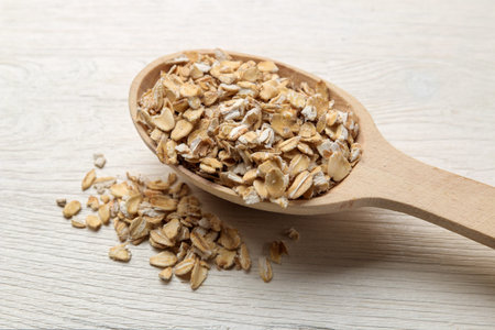 Dry oatmeal flakes in a wooden spoon on a white wooden table. healthy nutrition. healthy food.
