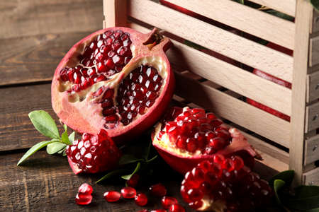 Ripe tasty red pomegranate fruit with leaves in a wooden box on a brown wooden table. close-upの写真素材