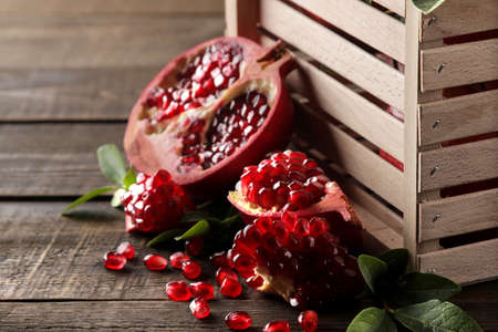 Ripe tasty red pomegranate fruit with leaves in a wooden box on a brown wooden table. close-upの写真素材