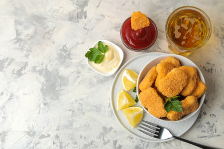 Chicken nuggets in a bowl with red sauce, ketchup and beer on a light concrete table. fast food. top...
