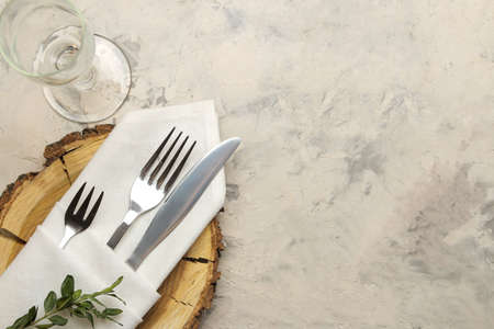 table setting. cutlery. glass, fork, knife in a white napkin and a wooden stand on a light concrete table. top viewの写真素材