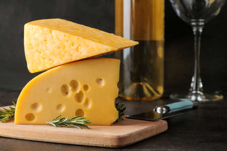 Slices of delicious marbled cheese and Maasdam cheese with white wine and rosemary on a dark background.の写真素材