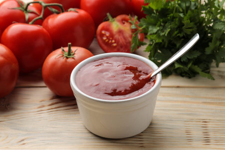 Red sauce or ketchup in a bowl and ingredients for cooking, tomatoes and herbs on a natural wooden...