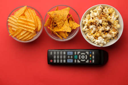 Popcorn with snacks and tv remote control on a bright red background. Concept of watching a movie or video at home. top viewの写真素材
