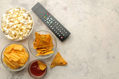 Popcorn and various snacks and a tv remote control on a light concrete table. Concept of watching a movie or video at home. top viewの写真素材