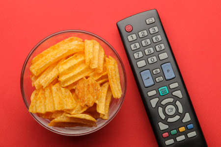Chips and tv remote control on a bright red background. Concept of watching a movie or video at home. top viewの写真素材