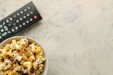 Popcorn and tv remote control on a light concrete table. Concept of watching a movie or video at...