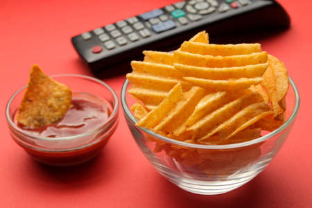 Chips and tv remote control on a bright red background. Concept of watching a movie or video at home.の写真素材