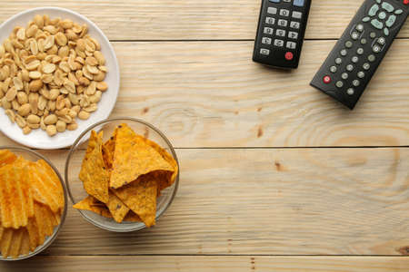 Chips and tv remote control on a natural wooden table. Concept of watching a movie or video at home. top viewの写真素材