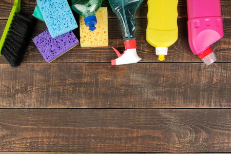 Different bottles with cleaning products and detergents and washcloths in a blue bucket on a brown...