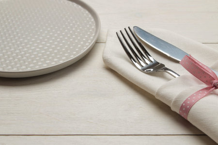 Table setting. plate and cutlery in a white napkin with a pink ribbon, fork and knife on a white...