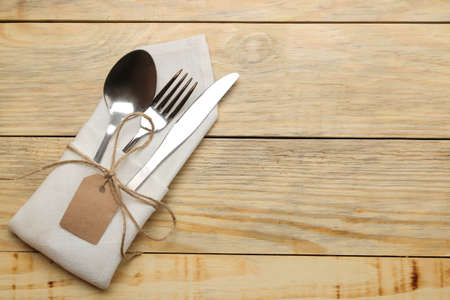 Table setting. Cutlery in a white napkin, fork, spoon and knife on a natural wooden table. top viewの写真素材