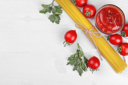 Pasta spaghetti with cherry tomatoes, red sauce and parsley on a white wooden background.