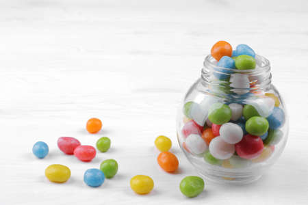 Multicolored round candy in a glass jar on a white wooden background.の写真素材