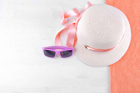 A summer hat with a pink ribbon and pink sunglasses on an orange towel. White wooden background, top view.の写真素材