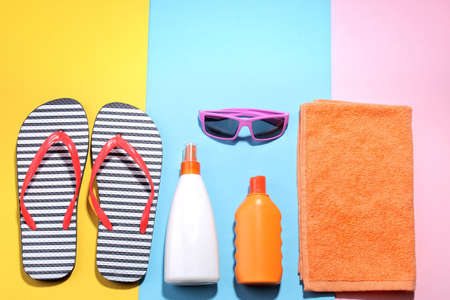 Beach accessories. Various creams, glasses, flip flops and a towel on a colored background. Top view.の写真素材