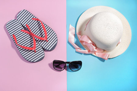 Beach accessories. Flip-flops and a summer hat with black sunglasses on a bright pink and blue...