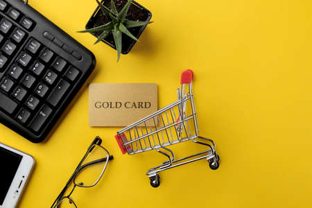 The concept of online shopping. Composition with a discount card and shopping trolley and telephone on a yellow backgroundの写真素材