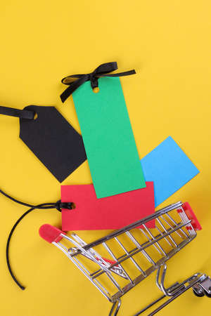 shopping trolley with multi-colored tags and price tags on a bright yellow background of the concept of black Friday. shopping. top viewの写真素材