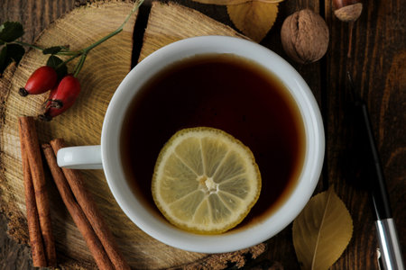 Autumn composition with hot tea on a wooden stand, cinnamon, dog rose, nuts on a brown wooden table....
