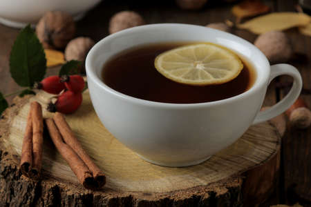 Autumn composition with hot tea on a wooden stand, cinnamon, dog rose, nuts on a brown wooden tableの写真素材