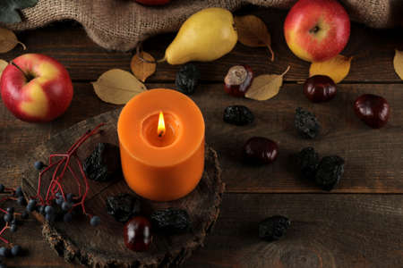 Autumn composition with candles and autumn fruits and berries and chestnuts on a brown wooden tableの写真素材