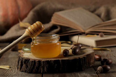 Autumn composition with honey close-up and acorns on a wooden stand on a brown wooden tableの写真素材